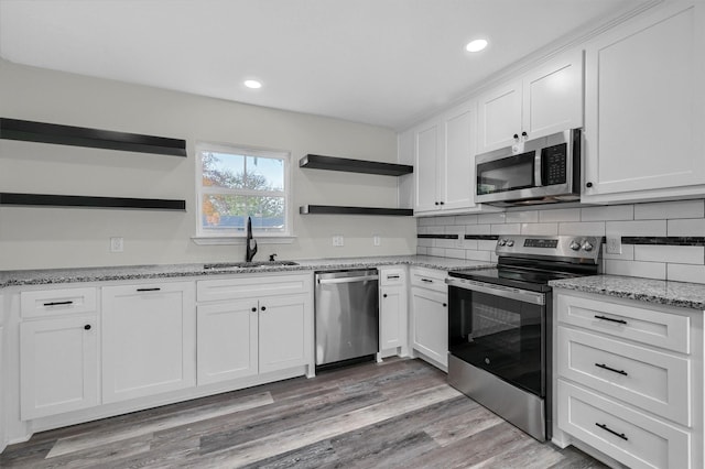 kitchen with white cabinetry, sink, stainless steel appliances, backsplash, and light wood-type flooring