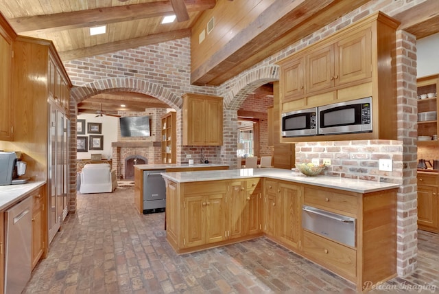 kitchen with vaulted ceiling with beams, a fireplace, kitchen peninsula, stainless steel appliances, and brick wall