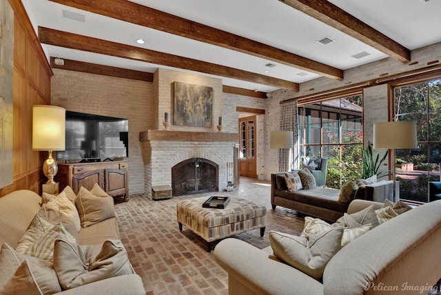 living room featuring beamed ceiling, a brick fireplace, and brick wall