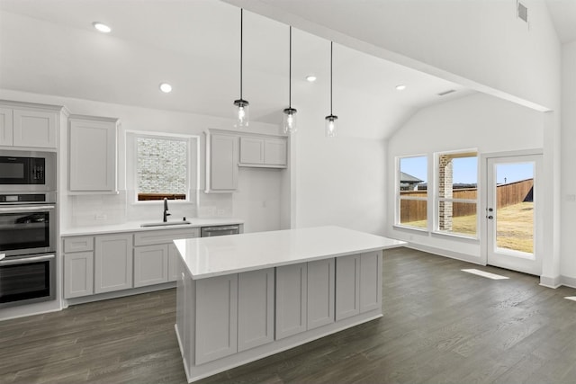 kitchen featuring decorative light fixtures, backsplash, vaulted ceiling, a kitchen island, and sink