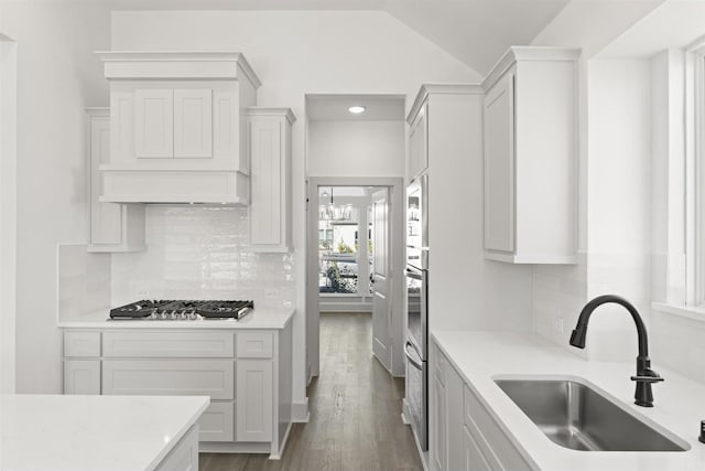 kitchen featuring vaulted ceiling, backsplash, sink, white cabinetry, and stainless steel gas cooktop