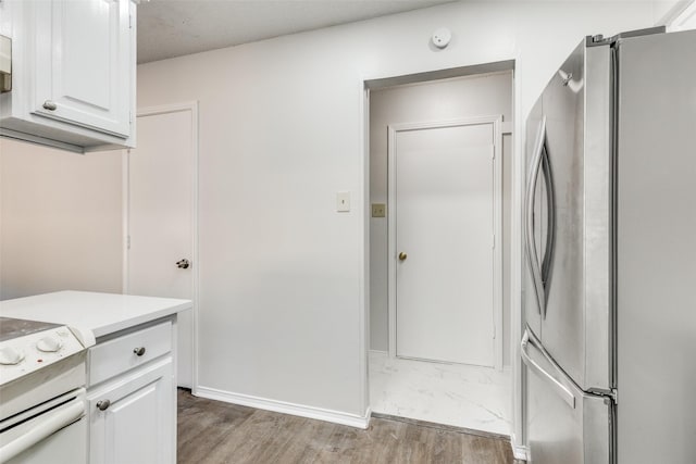 kitchen with light wood-type flooring, white cabinetry, stove, and stainless steel refrigerator