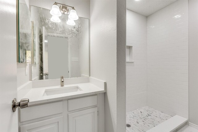 bathroom with a textured ceiling, vanity, and tiled shower