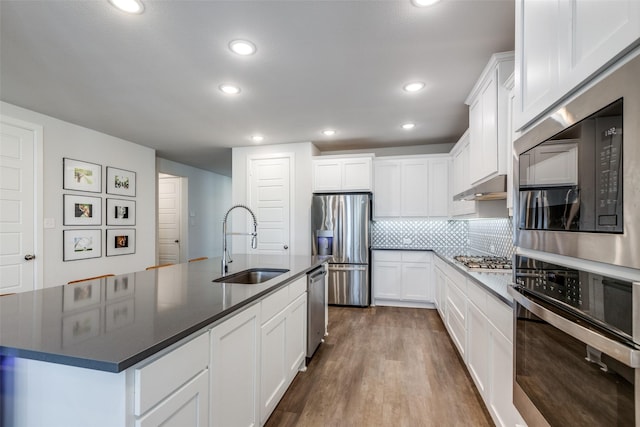 kitchen with appliances with stainless steel finishes, sink, a center island with sink, white cabinets, and hardwood / wood-style floors