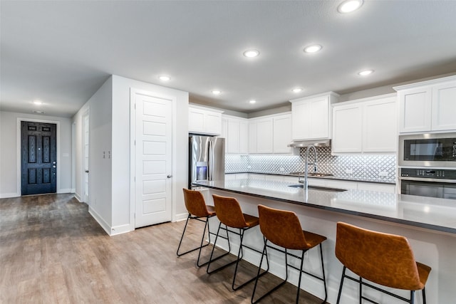 kitchen featuring white cabinets, a kitchen breakfast bar, sink, light wood-type flooring, and appliances with stainless steel finishes