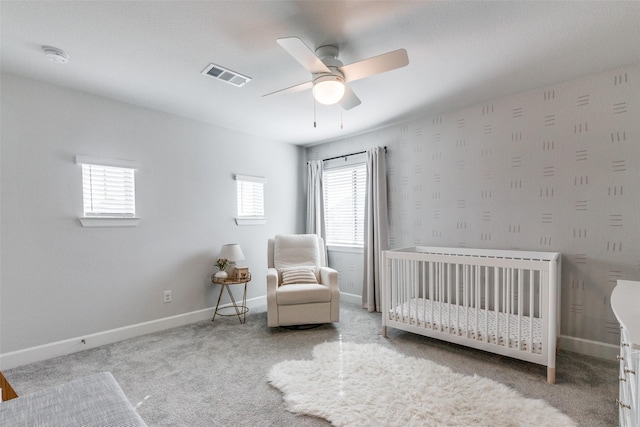 unfurnished bedroom with ceiling fan, a crib, and light carpet