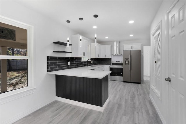 kitchen with kitchen peninsula, appliances with stainless steel finishes, wall chimney range hood, decorative light fixtures, and white cabinets