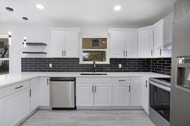 kitchen with light wood-type flooring, stainless steel appliances, sink, white cabinetry, and hanging light fixtures