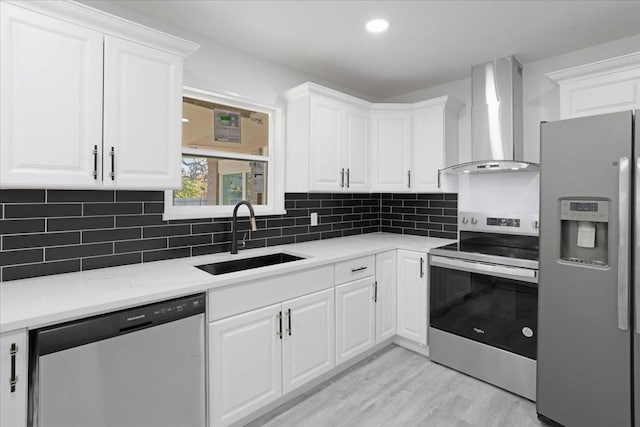 kitchen featuring white cabinetry, sink, wall chimney exhaust hood, light hardwood / wood-style flooring, and appliances with stainless steel finishes