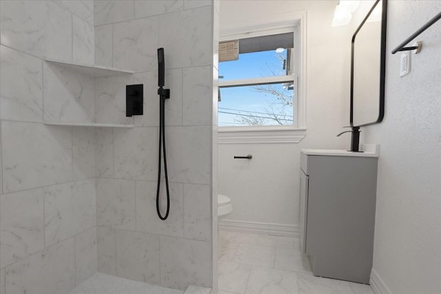 bathroom featuring a tile shower, vanity, and toilet