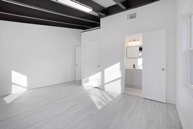 empty room featuring beam ceiling, light hardwood / wood-style flooring, and sink