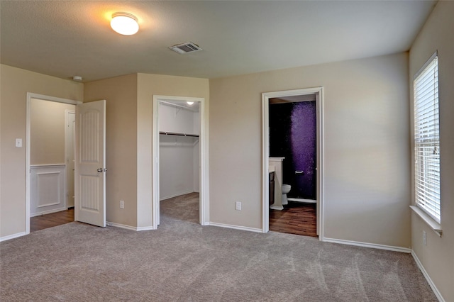 unfurnished bedroom featuring a walk in closet, light colored carpet, ensuite bath, and a closet