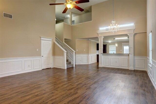 unfurnished living room with ceiling fan with notable chandelier, dark hardwood / wood-style flooring, and decorative columns