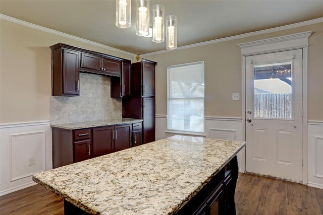 kitchen with pendant lighting, light stone countertops, ornamental molding, a kitchen island, and dark hardwood / wood-style flooring