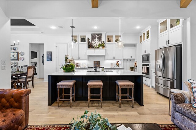 kitchen featuring appliances with stainless steel finishes, light wood-type flooring, a breakfast bar, pendant lighting, and an island with sink