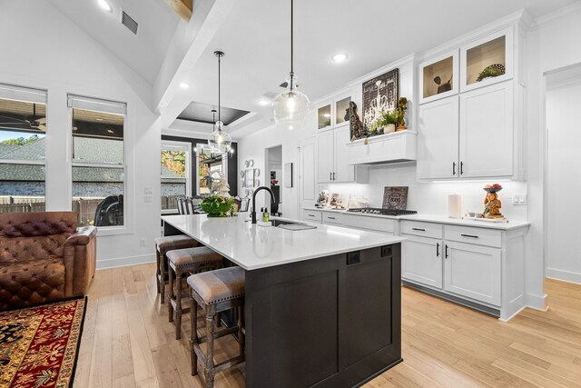 kitchen featuring sink, white cabinets, light hardwood / wood-style floors, hanging light fixtures, and an island with sink