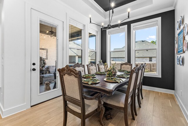 dining room featuring a raised ceiling, crown molding, light hardwood / wood-style flooring, and a notable chandelier