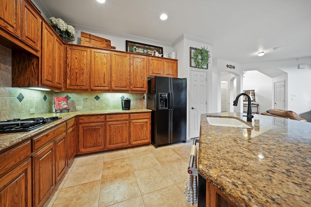 kitchen featuring light stone countertops, sink, backsplash, crown molding, and black fridge with ice dispenser