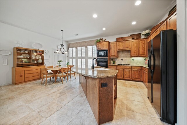 kitchen featuring decorative backsplash, a kitchen island with sink, black appliances, decorative light fixtures, and an inviting chandelier