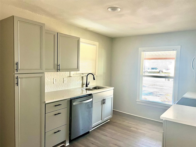 kitchen featuring backsplash, sink, light hardwood / wood-style flooring, stainless steel dishwasher, and gray cabinets