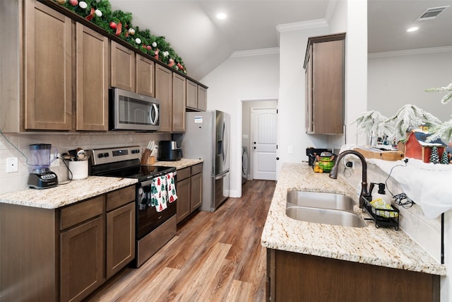 kitchen featuring backsplash, light stone counters, stainless steel appliances, crown molding, and sink