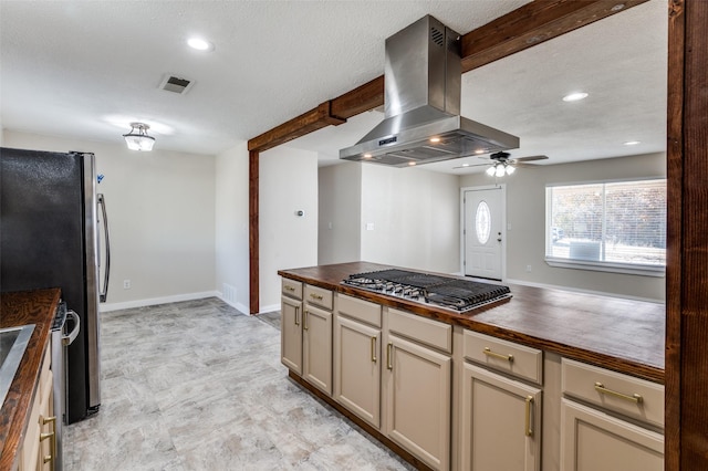 kitchen featuring wood counters, appliances with stainless steel finishes, ceiling fan, wall chimney range hood, and cream cabinetry