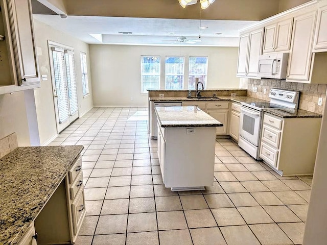 kitchen with kitchen peninsula, decorative backsplash, light stone countertops, white appliances, and a center island