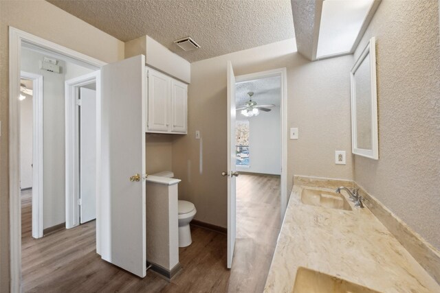 bathroom with ceiling fan, a textured ceiling, toilet, vanity, and hardwood / wood-style flooring