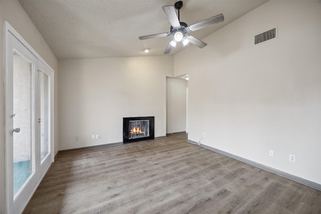 unfurnished living room with ceiling fan, lofted ceiling, a textured ceiling, and light hardwood / wood-style flooring