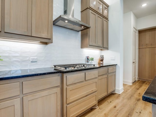 kitchen with range hood, backsplash, dark stone counters, stainless steel gas cooktop, and light hardwood / wood-style flooring