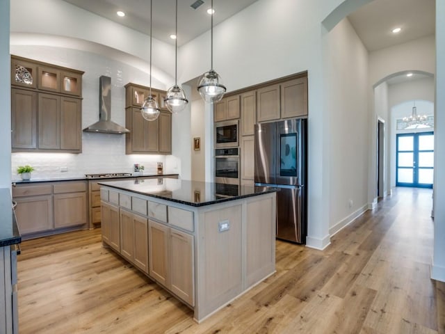 kitchen with wall chimney range hood, appliances with stainless steel finishes, a center island, decorative backsplash, and decorative light fixtures