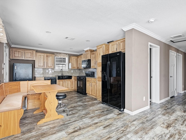 kitchen with backsplash, black appliances, ornamental molding, light brown cabinetry, and wood-type flooring