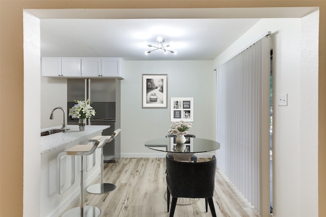 kitchen with sink, white cabinetry, light stone counters, light wood-type flooring, and stainless steel refrigerator