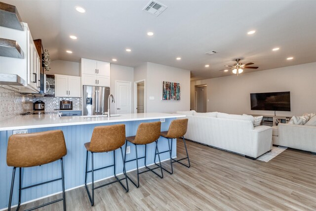 kitchen with white cabinetry, stainless steel appliances, tasteful backsplash, a kitchen breakfast bar, and light hardwood / wood-style flooring