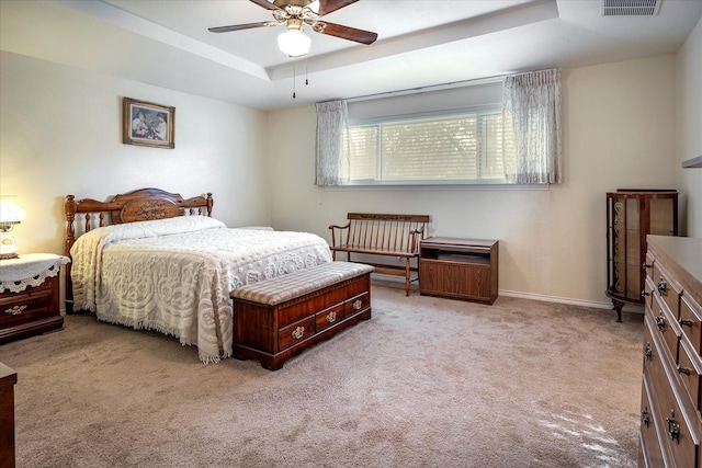 carpeted bedroom with ceiling fan and a tray ceiling