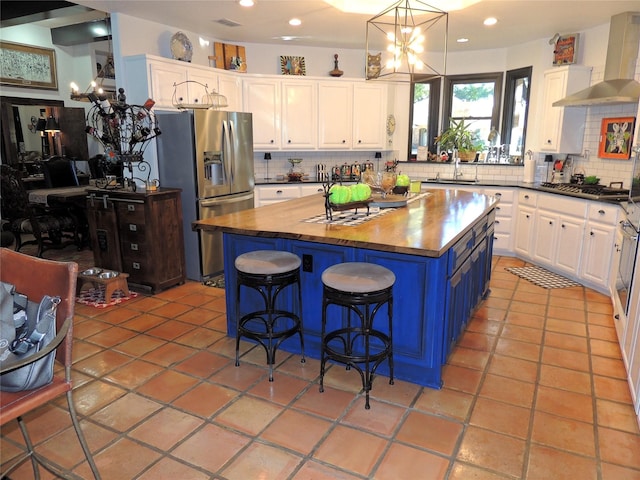 kitchen featuring butcher block countertops, white cabinetry, blue cabinets, a kitchen island, and wall chimney exhaust hood