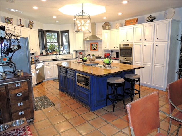 kitchen with wooden counters, stainless steel appliances, a center island, white cabinets, and blue cabinets