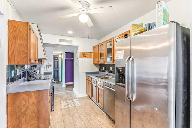 kitchen featuring appliances with stainless steel finishes, light wood-type flooring, backsplash, ceiling fan, and sink