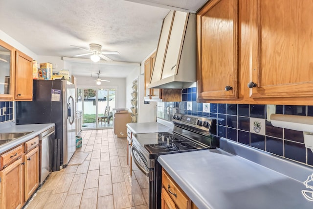 kitchen with ceiling fan, wall chimney range hood, backsplash, a textured ceiling, and appliances with stainless steel finishes