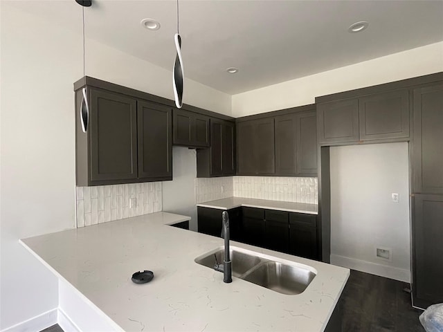 kitchen featuring kitchen peninsula, tasteful backsplash, sink, decorative light fixtures, and hardwood / wood-style floors