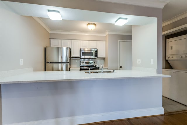 kitchen featuring kitchen peninsula, stacked washing maching and dryer, stainless steel appliances, hardwood / wood-style flooring, and white cabinets