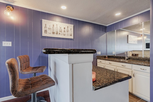 kitchen with a textured ceiling, wood walls, white cabinetry, and sink