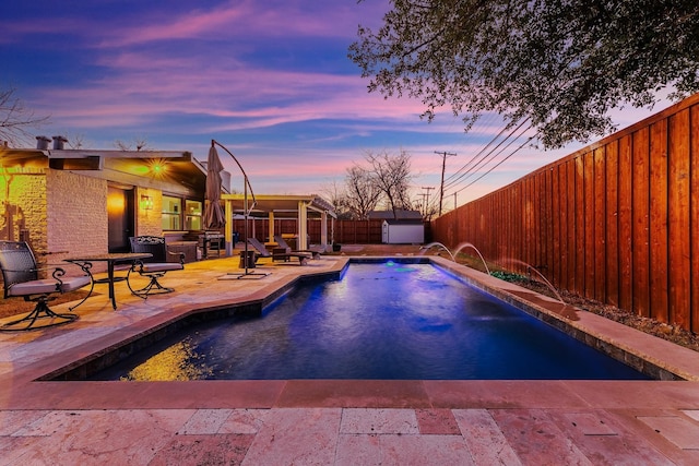 pool at dusk with a patio area and pool water feature