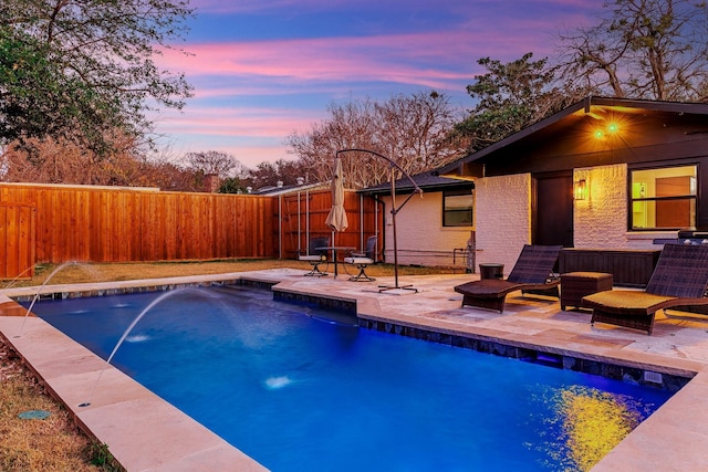 pool at dusk featuring pool water feature and a patio