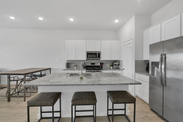 kitchen featuring white cabinets, light wood-type flooring, a kitchen island with sink, and appliances with stainless steel finishes