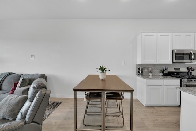 kitchen with white cabinets, decorative backsplash, light stone countertops, light wood-type flooring, and appliances with stainless steel finishes