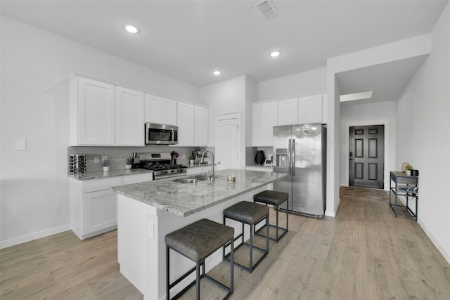 kitchen with white cabinetry, sink, light stone counters, a kitchen island with sink, and appliances with stainless steel finishes