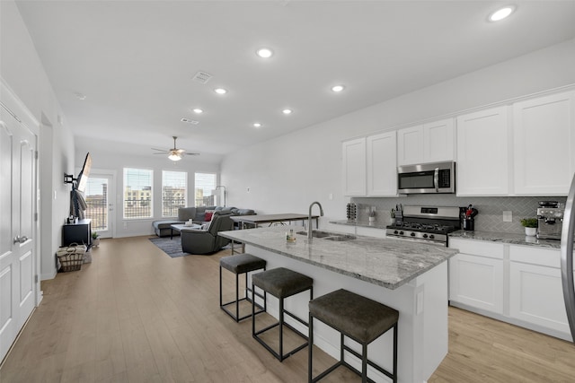 kitchen featuring appliances with stainless steel finishes, a kitchen island with sink, ceiling fan, white cabinets, and light hardwood / wood-style floors