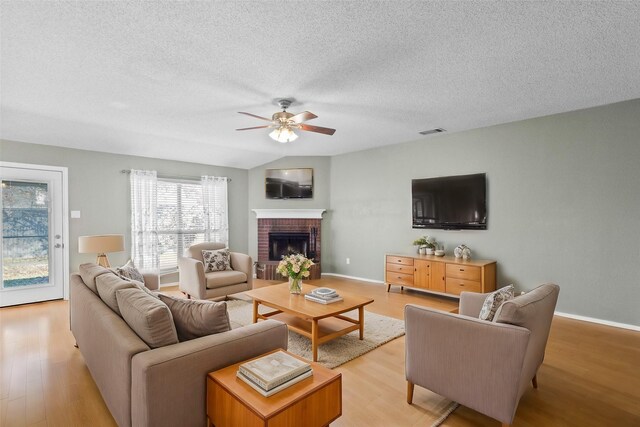 living room featuring ceiling fan, a brick fireplace, light hardwood / wood-style flooring, a textured ceiling, and vaulted ceiling