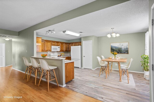 kitchen with light hardwood / wood-style floors, white appliances, kitchen peninsula, and a chandelier